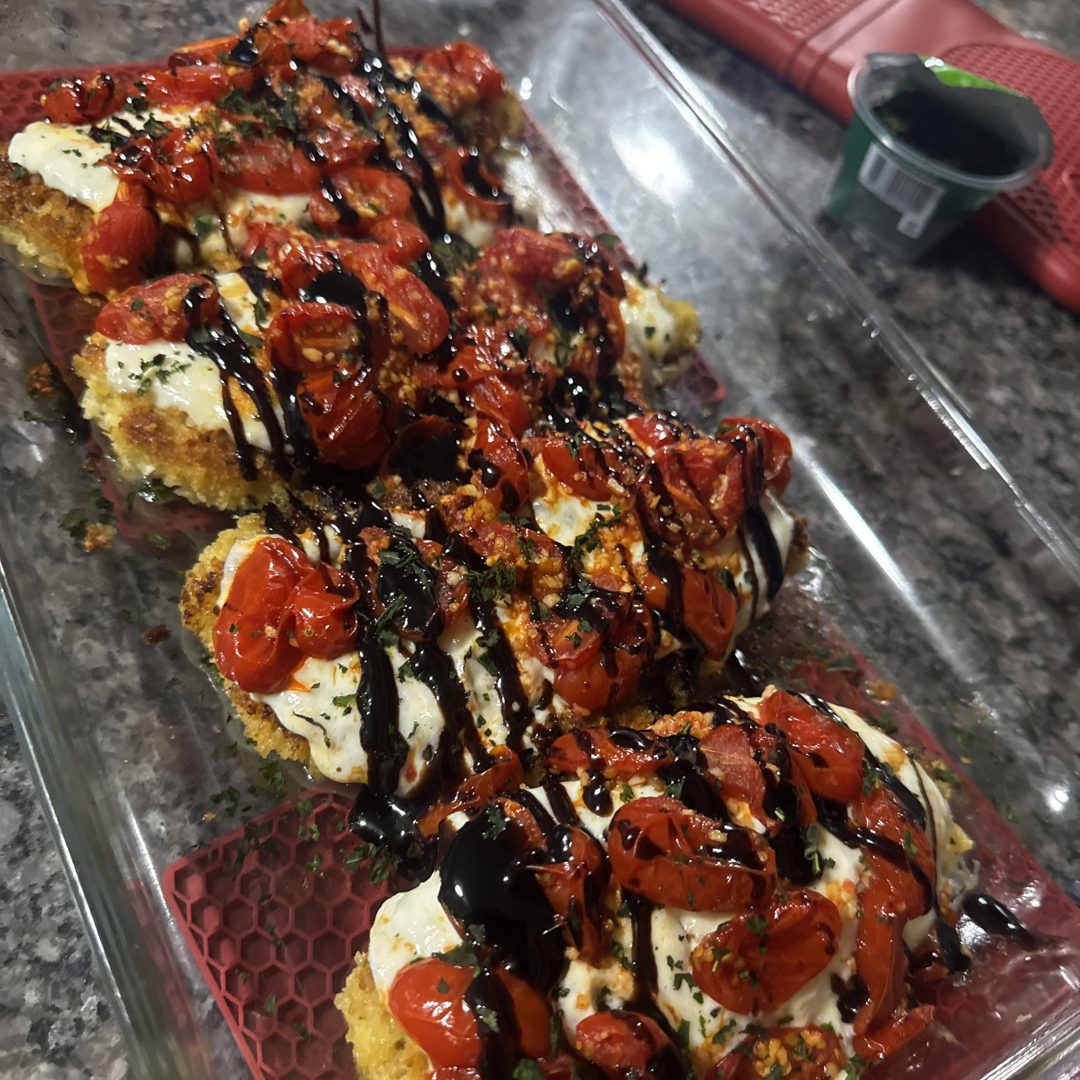 Breaded chicken topped with mozzarella, roasted cherry tomatoes and balsamic glaze, in a glass baking dish.