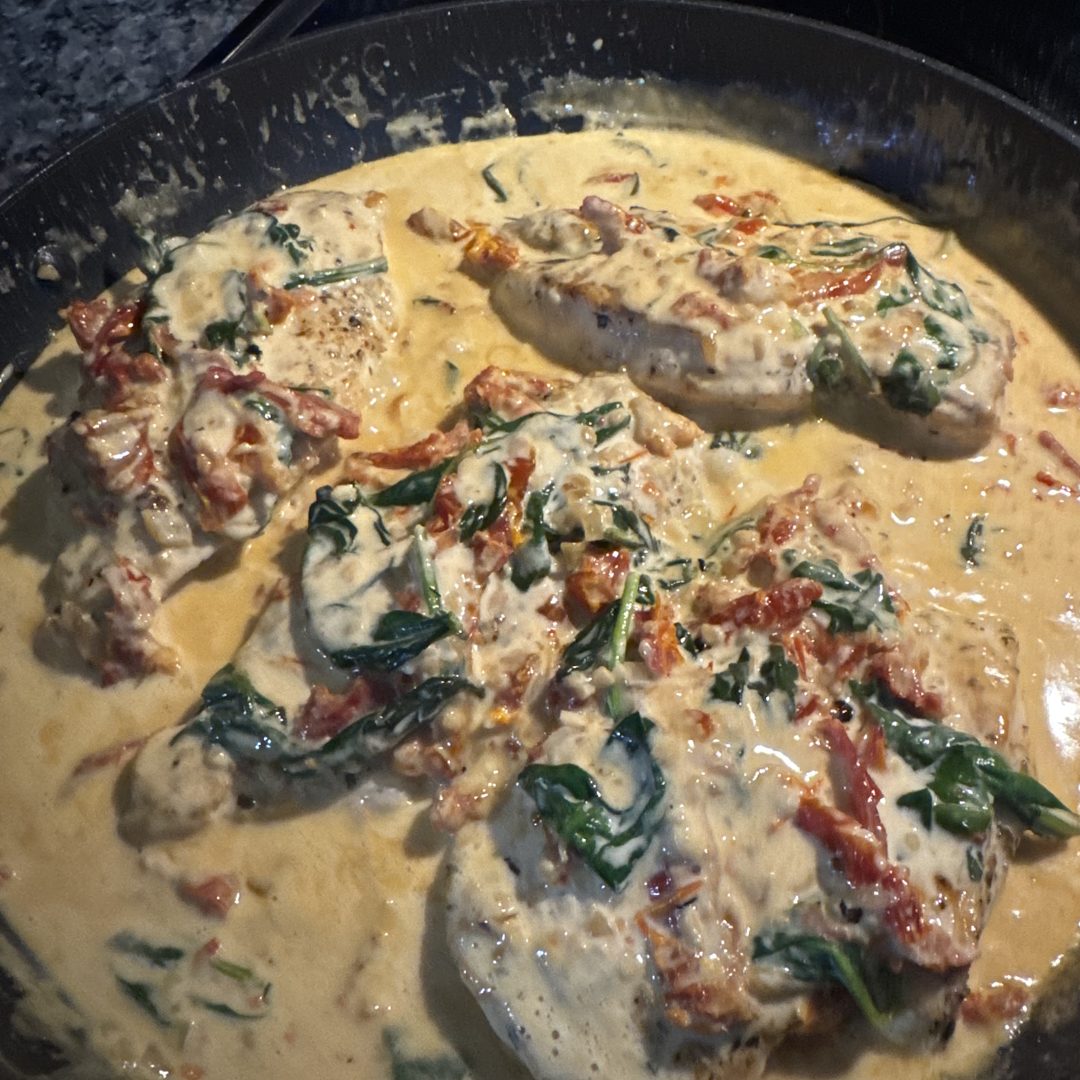 Chicken in a creamy sauce with spinach and sun-dried tomatoes, in a skillet.